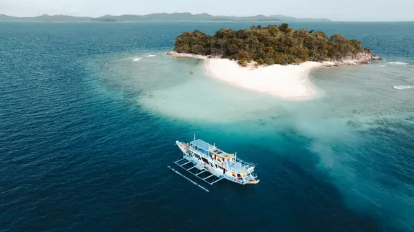 Aerial drone view of the Seatours expedition boat anchored off a white-sand island with turquoise lagoon, private 3D2N Palawan charter route