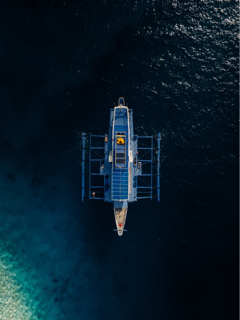 Aerial top-down of a Seatours Palawan expedition bangka over deep blue water and reef